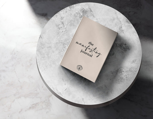 How to write manifestations: cover of The Manifesting Journal displayed on a marble round table